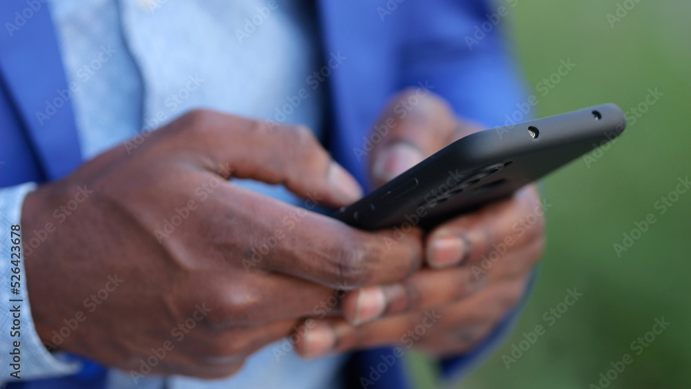 Black man wearing blue blazer hands enter necessary information into modern smartphone. African American person works as entrepreneur outdoors