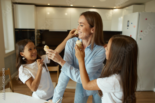 Young beautiful mother and her daughters have fun together. A beautiful woman and her little children are preparing ice cream. Family having fun, eating ice cream balls, stained with cream