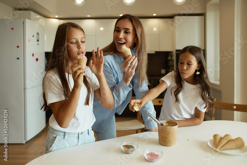 Young beautiful mother and her daughters have fun together. A beautiful woman and her little children are preparing ice cream. Family having fun, eating ice cream balls, stained with cream
