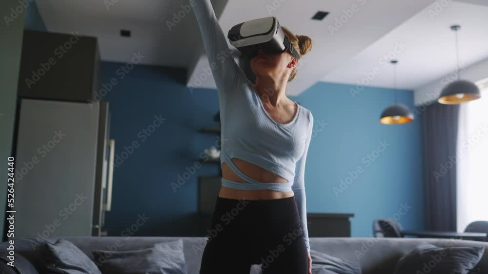 Futuristic girl funny dancing in VR headset for social media platform media in living room at home. Woman avatar performing in metaverse cyberspace immersive experience for followers audience. Futuristic girl funny dancing in VR headset for social media platform media in living room at home. Woman avatar performing in metaverse cyberspace immersive experience for followers audience.