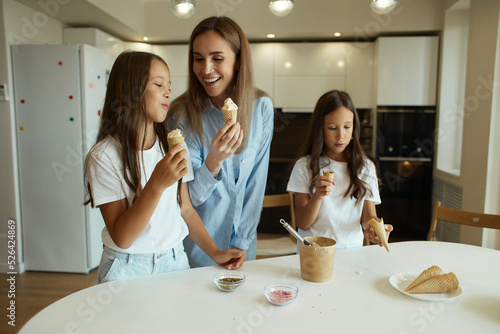 Young beautiful mother and her daughters have fun together. A beautiful woman and her little children are preparing ice cream. Family having fun, eating ice cream balls, stained with cream