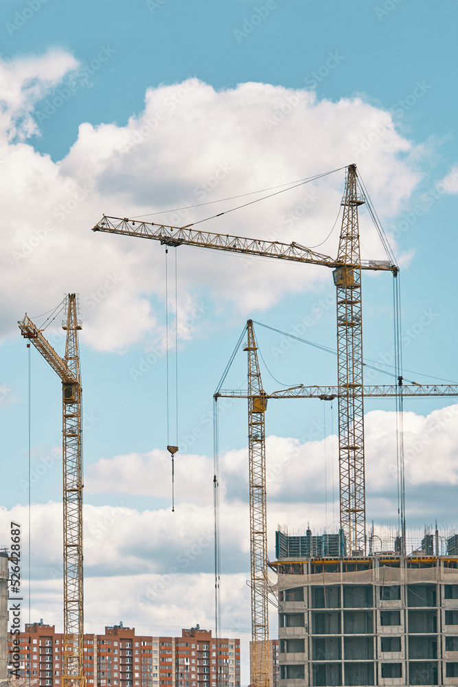 Industrial building cranes on background of cloudy sky. Hoisting cranes and multi-storey buildings of new city districts. Construction site background. Industrial building cranes on background of cloudy sky. Hoisting cranes and multi-storey buildings of new city districts. Construction site background.