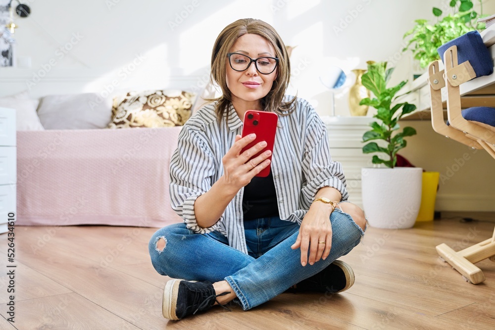 Middle aged woman sitting on floor at home with smartphone Middle aged woman sitting on floor at home with smartphone