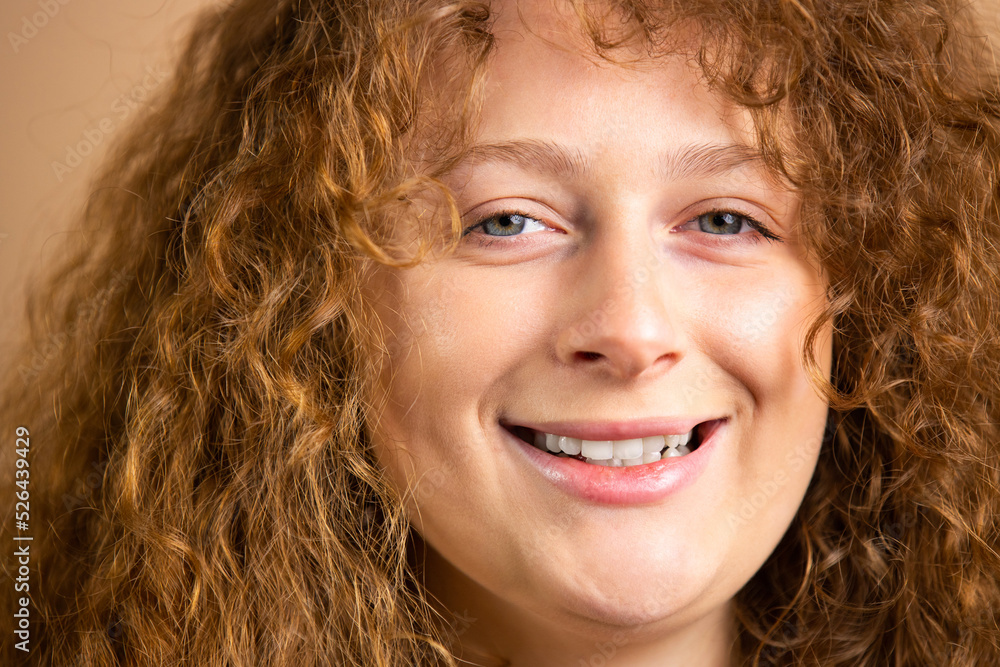 Happy smiling flirty glance portrait of curly redhead young woman with blue eyes over a golden background. Happy smiling flirty glance portrait of curly redhead young woman with blue eyes over a golden background.