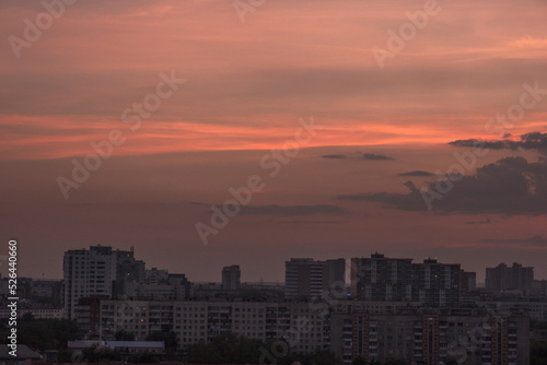 Sunset with gold, red, yellow and orange sunlight coming through the clouds, in a city among tall black houses. Horizontal photograph. Nature. Architecture.