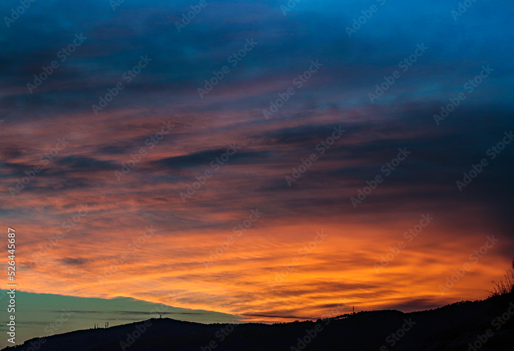 cloudy sunset with orange clouds and mountain silhouettes
