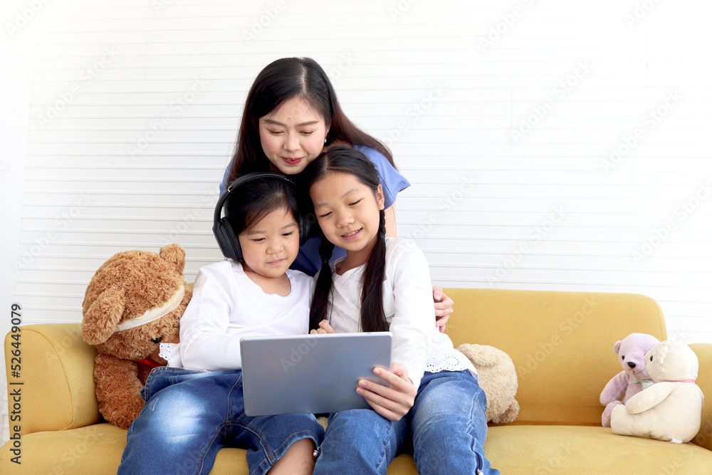 Adorable Asia happy family, cute two daughter girls with mother hold digital tablet, looking at web camera, smiling mom and children have fun meeting online. Family surfing internet.