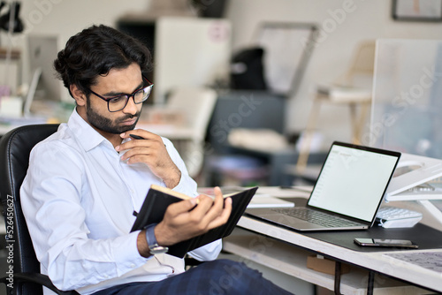 Busy indian business man planning agenda looking in notebook organizer thinking on calendar daily appointments and tasks making schedule working in office managing sitting at workplace.