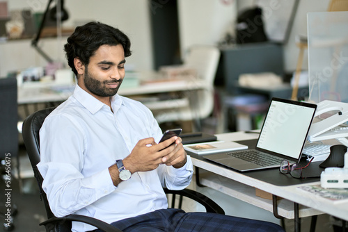 Indian young business man company worker  professional employee  stock market trader holding smartphone using cell phone mobile apps reading news  checking financial market data at work in office.