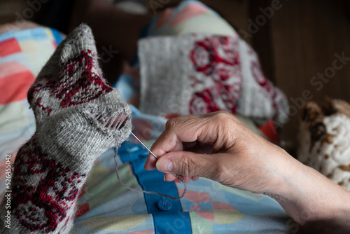 Close up of old lady hands darning winter socks with hole. Poverty in world economic crisis concept 