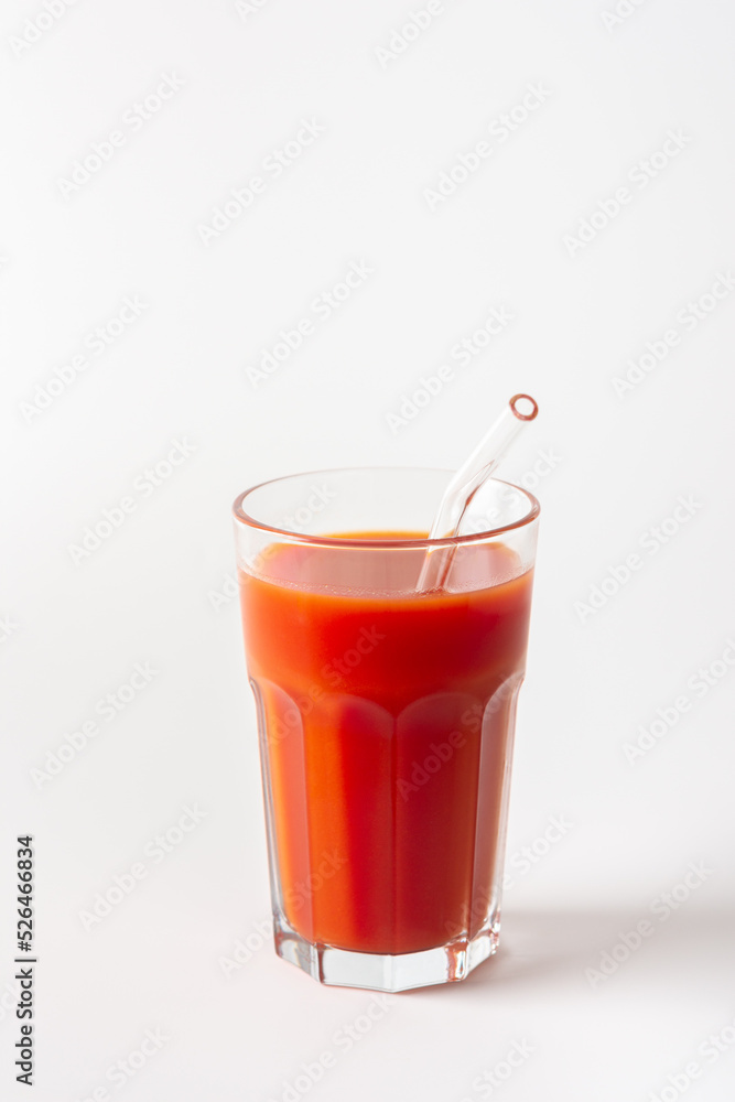 Homemade freshly squeezed tomato juice in a glass with a glass straw close-up on a white background Homemade freshly squeezed tomato juice in a glass with a glass straw close-up on a white background