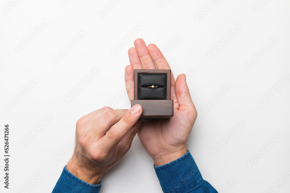 a man's hand holds a diamond engagement ring in a wooden elegant box, making a marriage proposal a man's hand holds a diamond engagement ring in a wooden elegant box, making a marriage proposal