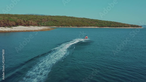 Young man in red swimming suit enjoying his holiday riding electric surfboard in a calm blue ocean bay between yachts and sailboards. Summer sport for friends. photo