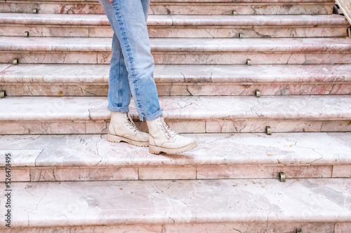 Woman's legs in blue twisted jeans and in beige boots on pink marble staircase. Front view