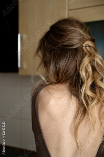 Woman with long blond styled hair wearing dress with open back standing turned away