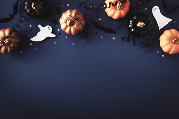 Halloween holiday background with party decorations of pumpkins, bats, ghosts on dark blue table top view. Happy halloween greeting card in flat lay style.