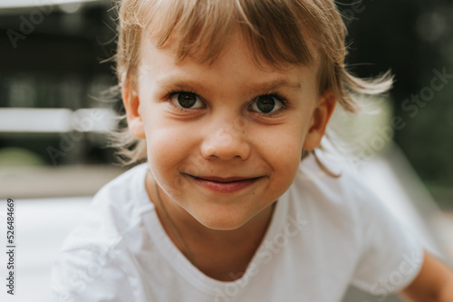 portrait of the face of a cute little happy smiling candid five year old kid boy with big eyes and long blond hair in a white t-shirt. generation z children mental health lifestyle and mind psychology