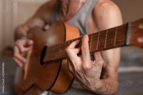 male hands of an elderly senior caucasian man holding and playing a classical guitar close up at home. unprofessional faceless guitarist people play amateur music. domestic hobbies and leisure