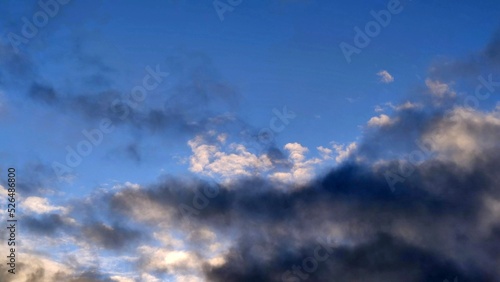 Sky with dark clouds. Autumn day the sky is blue. There are clouds in the sky at different levels. White fluffy clouds above, dark gray below. They are of different shapes and sizes.