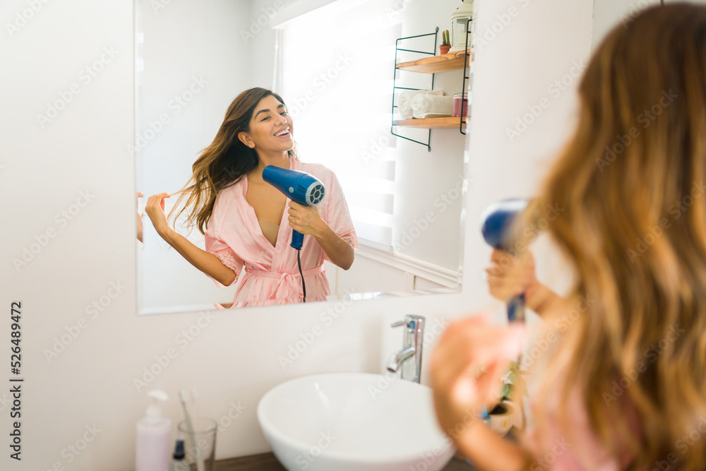 Rear view of a cheerful young woman blow drying her hair Rear view of a cheerful young woman blow drying her hair
