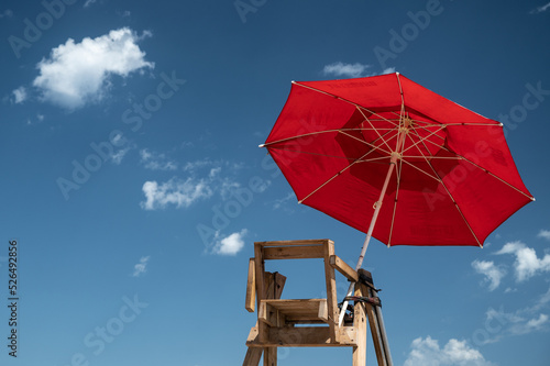 Chair and red SOS umbrella of a lifeguard in a beach against blue sky with copy space