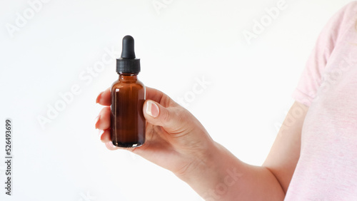 Woman's hand hold natural skincare serum in dropper bottle on white background . Cosmetic beauty background.