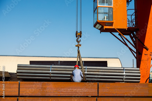 Worker preparing stack of metal pipes for transporting with gantry crane photo
