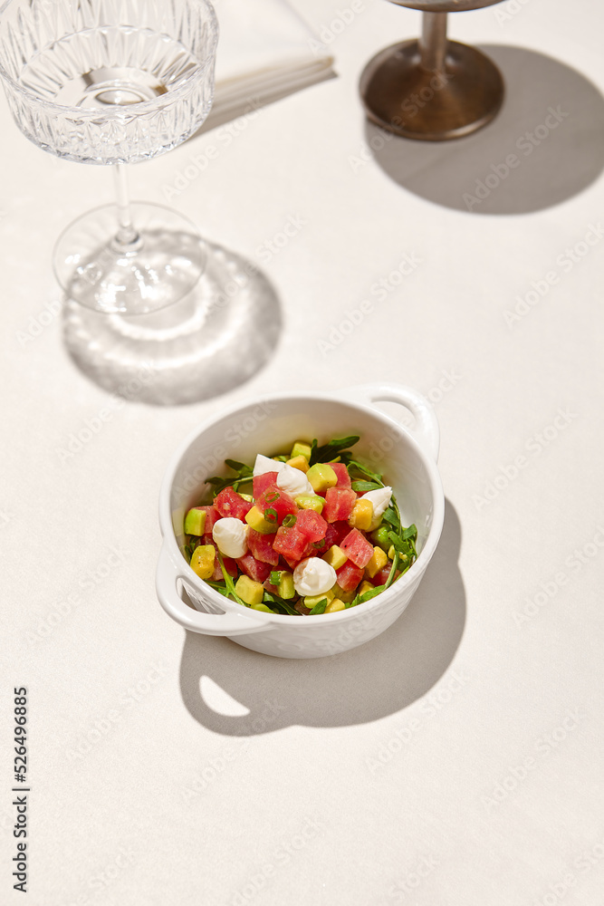 Tuna tartar in ceramic bowl on white table in sunny day. Tuna and avocado tartar with cream cheese in restaurant menu. Appetizer from tuna and avocado with shadow from wine glass. Tuna tartar in ceramic bowl on white table in sunny day. Tuna and avocado tartar with cream cheese in restaurant menu. Appetizer from tuna and avocado with shadow from wine glass.