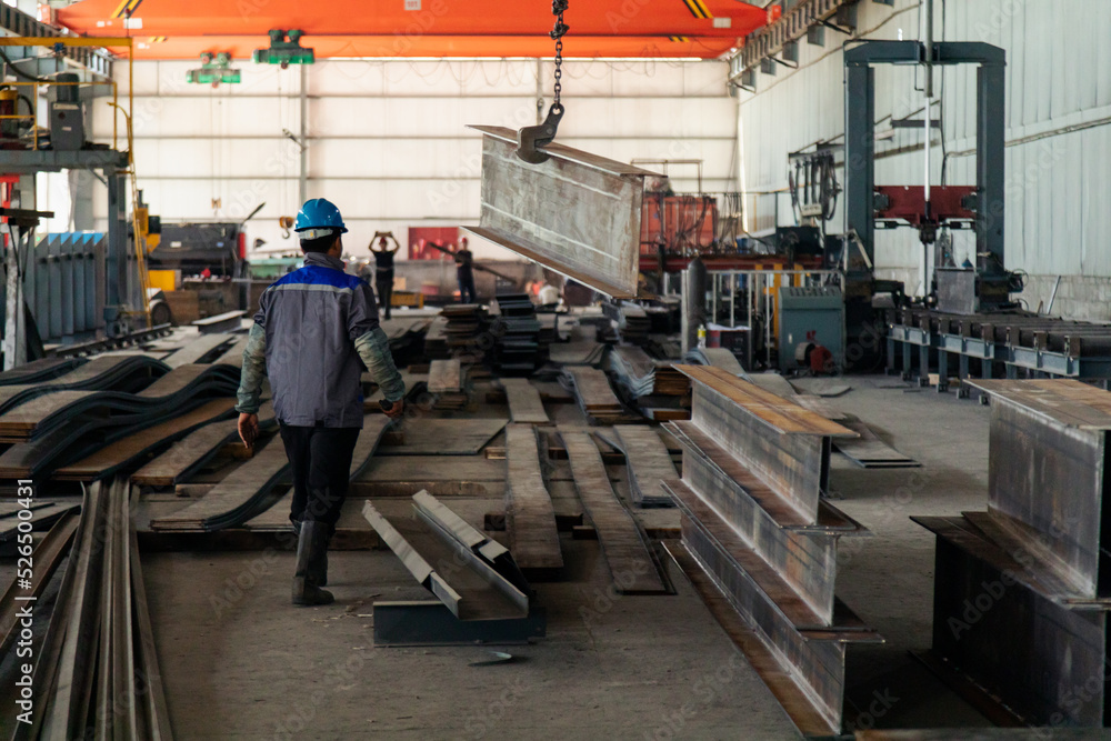 Fototapeta premium Worker receiving a metal bar from crane in warehouse