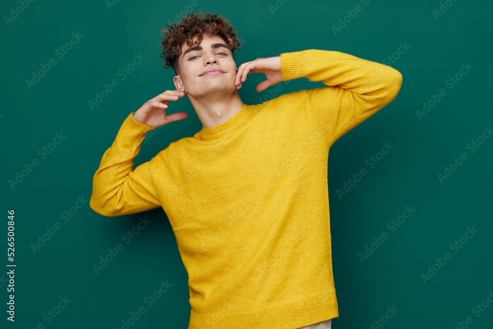 a relaxed man with curly hair, standing on a green background in a yellow sweater and closing his eyes holding his head with his hands a relaxed man with curly hair, standing on a green background in a yellow sweater and closing his eyes holding his head with his hands