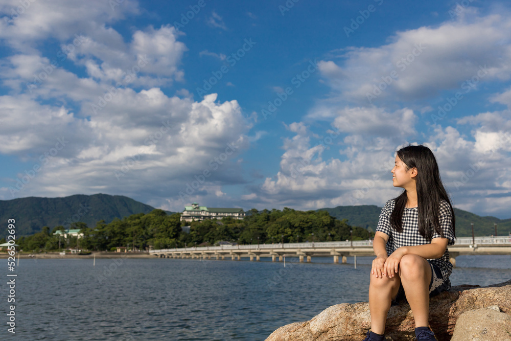 海岸の岩に座って海を眺める女子学生の姿