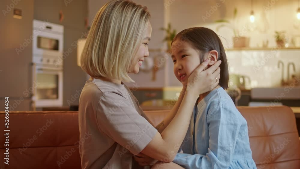 Portrait of a Mother Lovingly Embracing her Daughter. Mother Parent Hugging her Kid Having a Tender and Lovely Moment in Living Room at Home. Mother's Day concept Portrait of a Mother Lovingly Embracing her Daughter. Mother Parent Hugging her Kid Having a Tender and Lovely Moment in Living Room at Home. Mother's Day concept