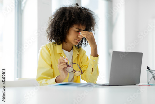 Tired frustrated black woman working in the office, sitting at the table and using a laptop computer