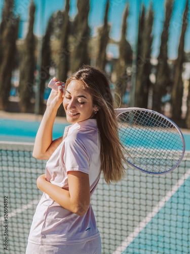 Mujer joven sonriente usando una raqueta de tenis en una pista de tenis al aire libre durante las vacaciones de verano