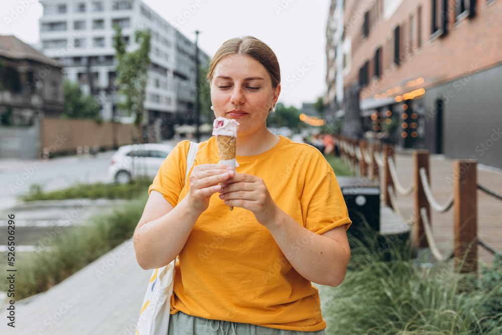 Fototapeta premium Happy attractive woman on the street having fun and eating ice cream. Young smiling girl dressed in yellow t-shirt holding ice cream. Food banner