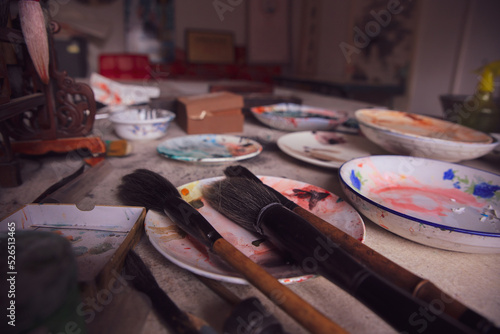 Paint brushes of a traditional chinese calligraphy painter artist standing on the table in a plate with other oil paints around