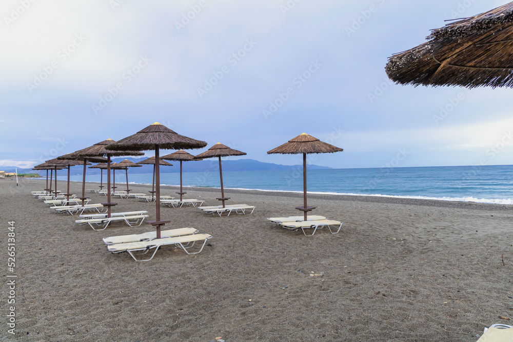 Empty beach with sun loungers and umbrellas in the early morning and a cloudy sky. Crete Greece. High quality photo