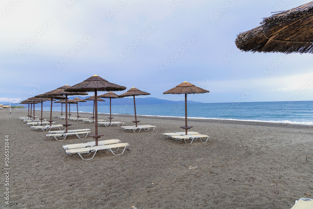 Fototapeta premium Empty beach with sun loungers and umbrellas in the early morning and a cloudy sky. Crete Greece. High quality photo