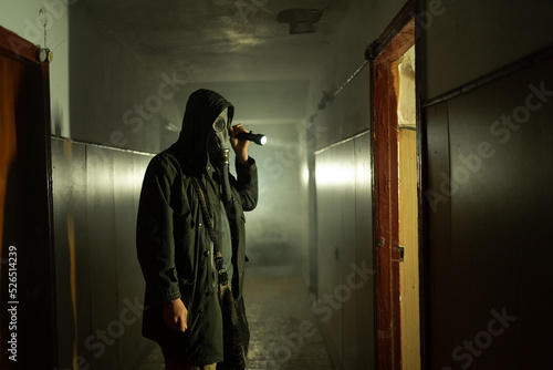 Man in respirator gas mask with flashlight inside of abandoned building in dark. Cyberpunk postapocalypse fantasy horror scene, or air pollution photo