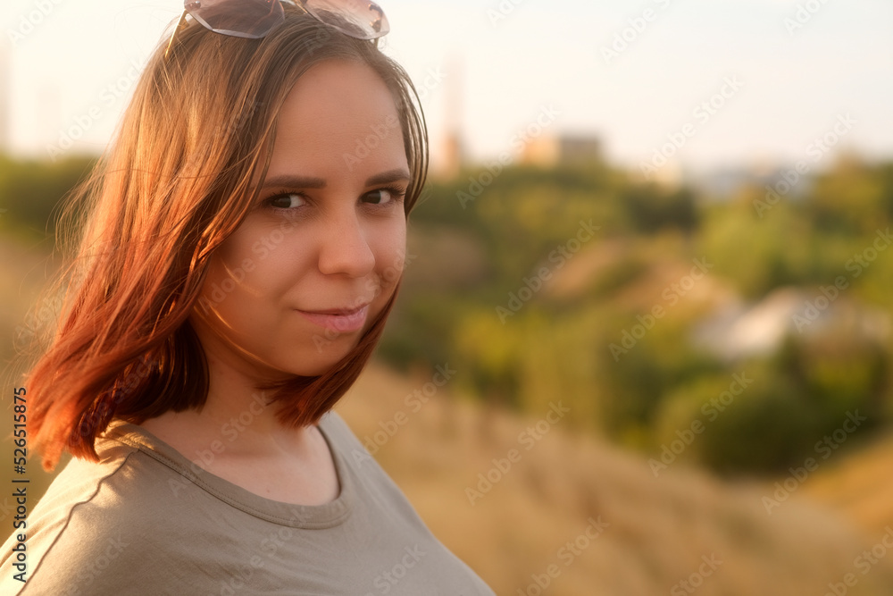 Young woman with flying hair looking at camera while standing on blurred background of meadow