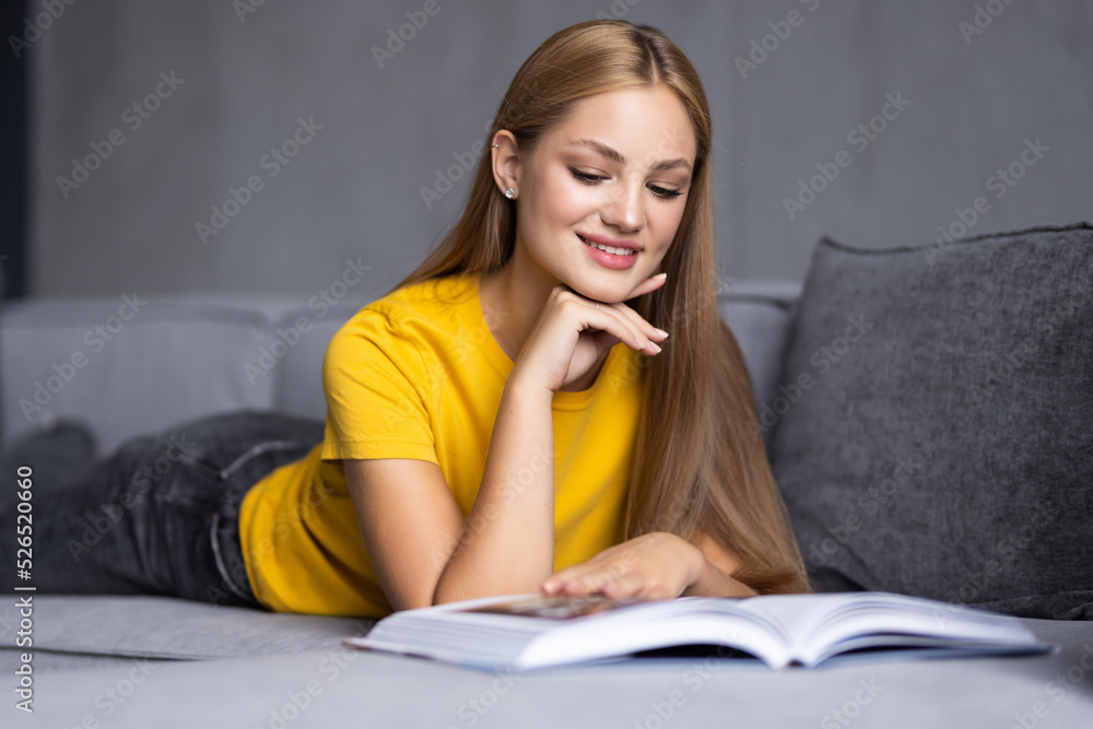 Happy young woman reading storybook on couch at home Happy young woman reading storybook on couch at home