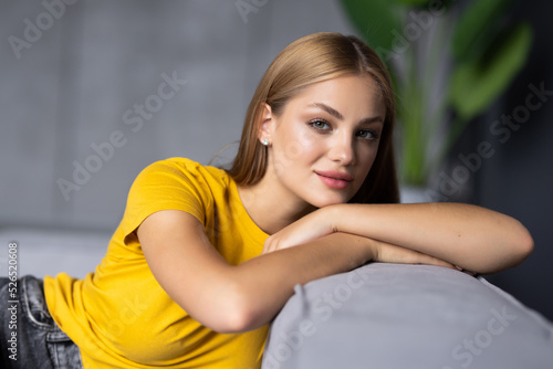 Smiling pretty young woman wearing casual clothes relaxing on a couch at home