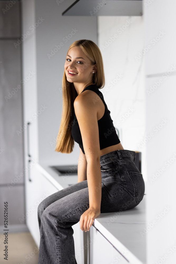 Young woman looking at camera while sitting on the kitchen counter Young woman looking at camera while sitting on the kitchen counter