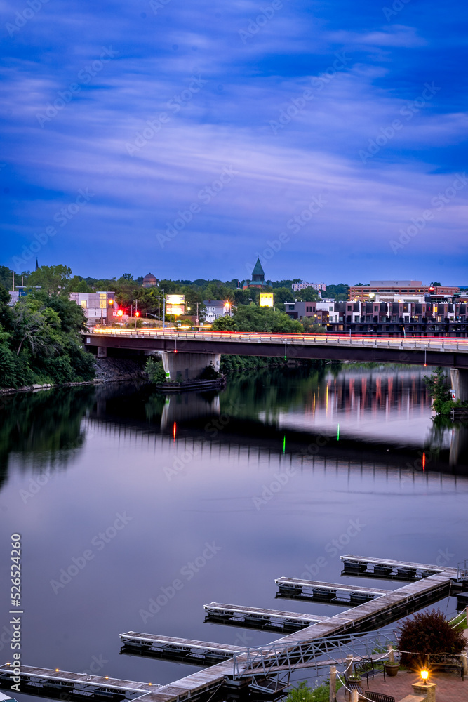 Schenectady, NY - USA - Aug 1, 2022  vertical view during the blue hour of Schenectady’s skyline, with the Freemans Road Bridge and the Mohawk River in the foreground