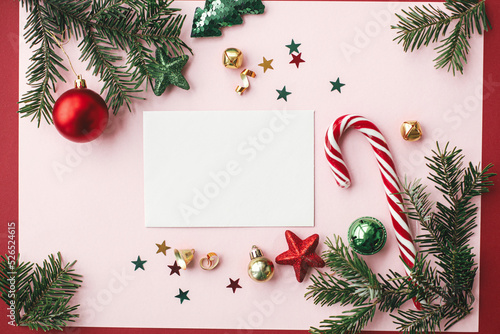 Christmas card mockup. Empty greeting card flat lay with red christmas decorations, fir branches and ornaments on pink background. Modern Postcard template with space for text. Happy Holidays!