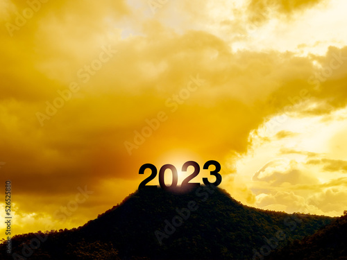 Happy New year 2023 with large silhouette letters on the mountain with beautiful sunset light, sunlight, golden sky and clouds for success concept. Welcome Merry Christmas and Happy New Year in 2023.