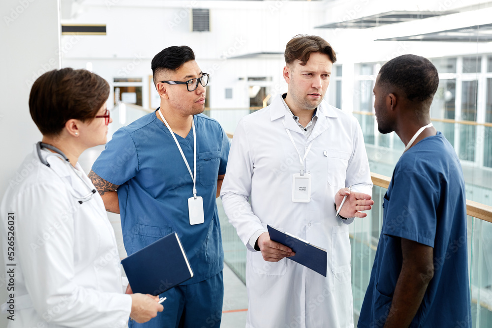 Diverse group of doctors standing in circle and discussing work in modern clinic Diverse group of doctors standing in circle and discussing work in modern clinic