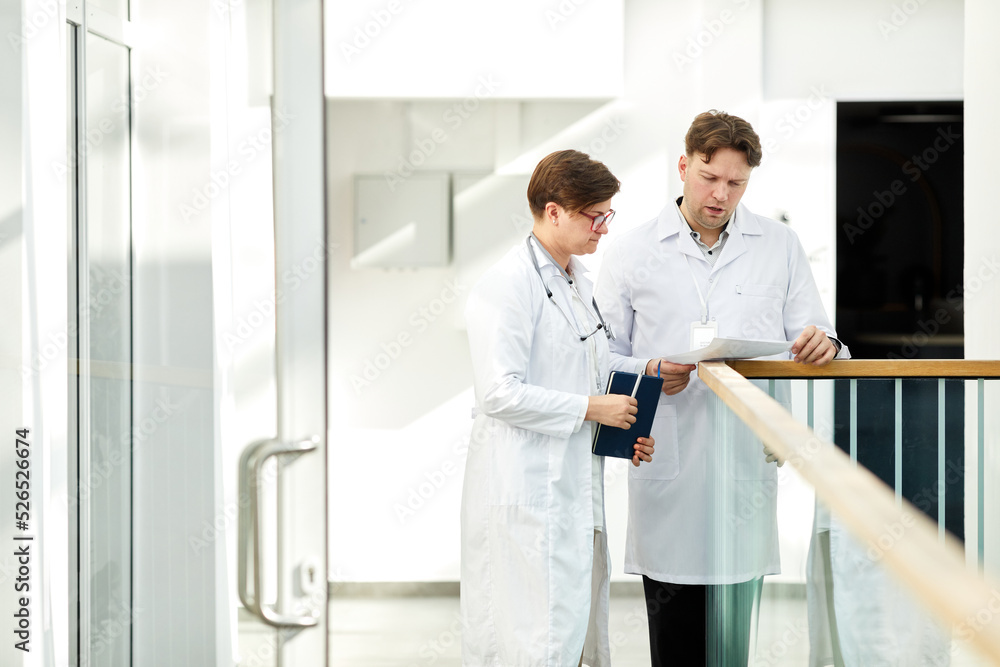 Obraz premium Minimal portrait of two expert doctors discussing case in hall of modern clinic in white tones, copy space