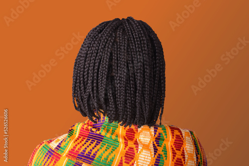 African woman with short braided hair wearing traditional Kente wrap on orange background photo
