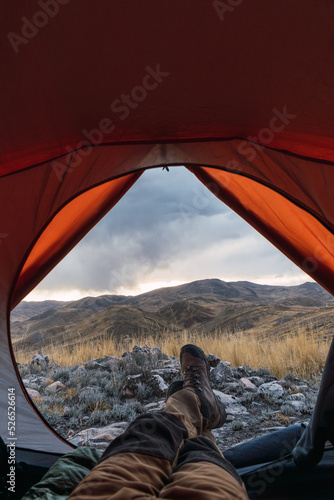 man's feet with boots inside an orange tent in the mountains in a sunset surrounded by rocks and yellow vegetation in the winter in the andes mountain range